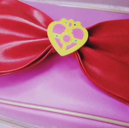 pink sailor moon makeup bag with large red bow handle, wand designs and gold zipper